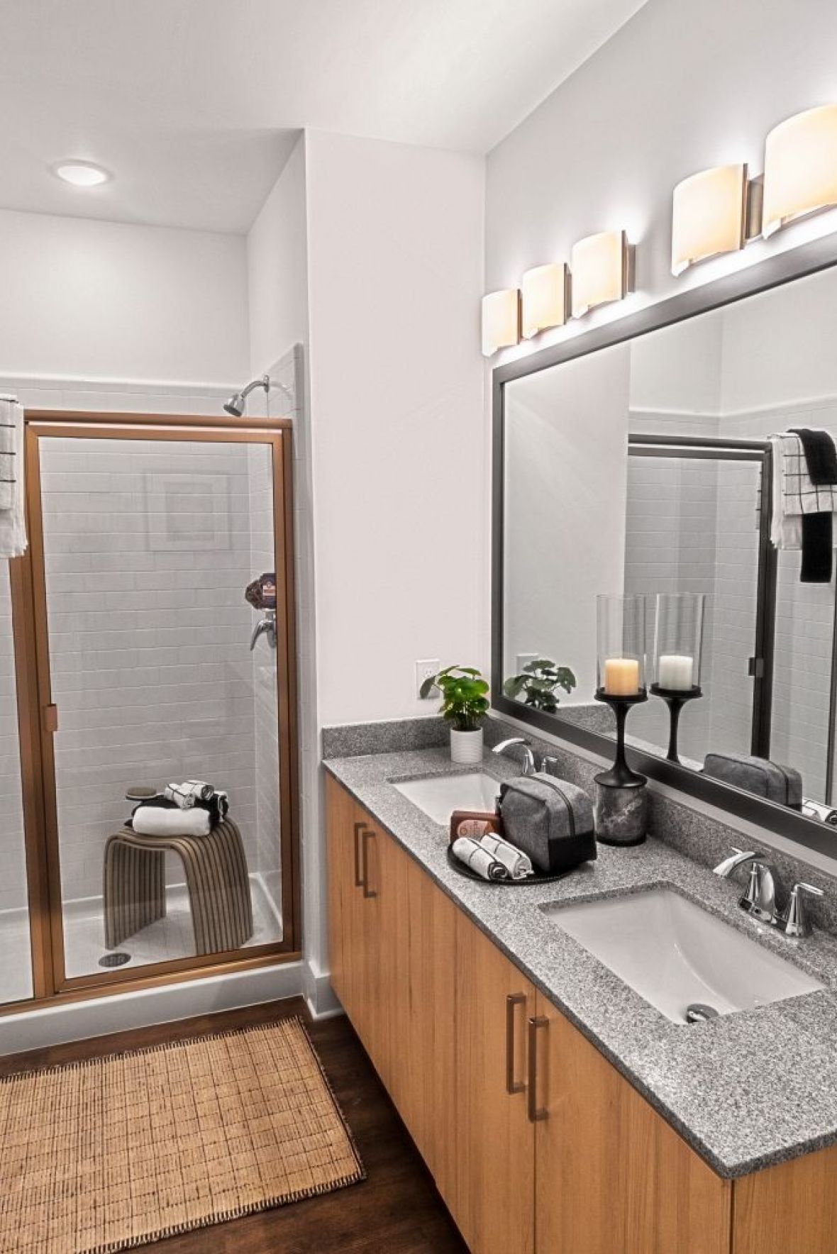 Modern bathroom with glass shower, large vanity mirror, candles, and towels on wooden cabinets and countertop at The Fieldhouse Apartments.