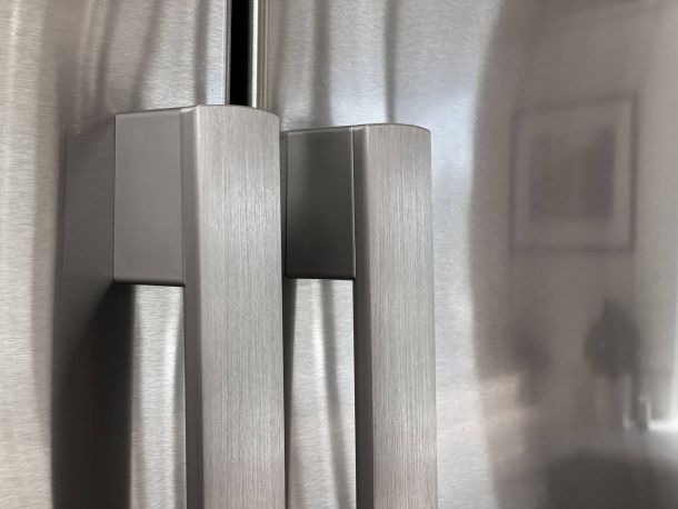 Close-up of two stainless steel refrigerator door handles with a soft reflection in the background.
