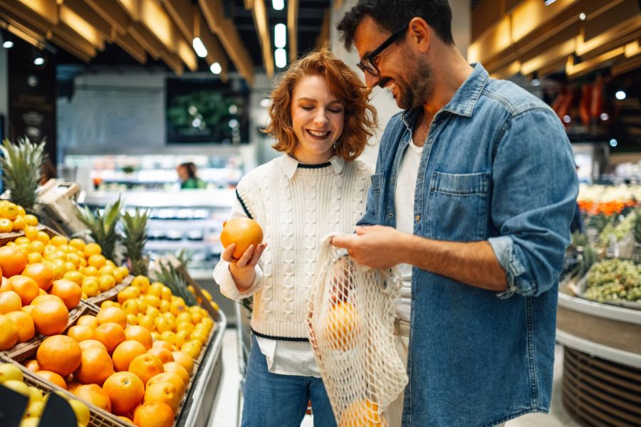 A smiling couple shops for oranges together in the produce section of a grocery store.