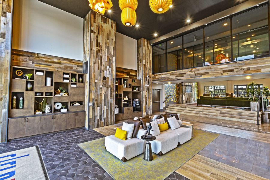 Modern lobby with wooden accents, a white sofa, yellow pillows, and large hanging lights at The Fieldhouse Apartments.
