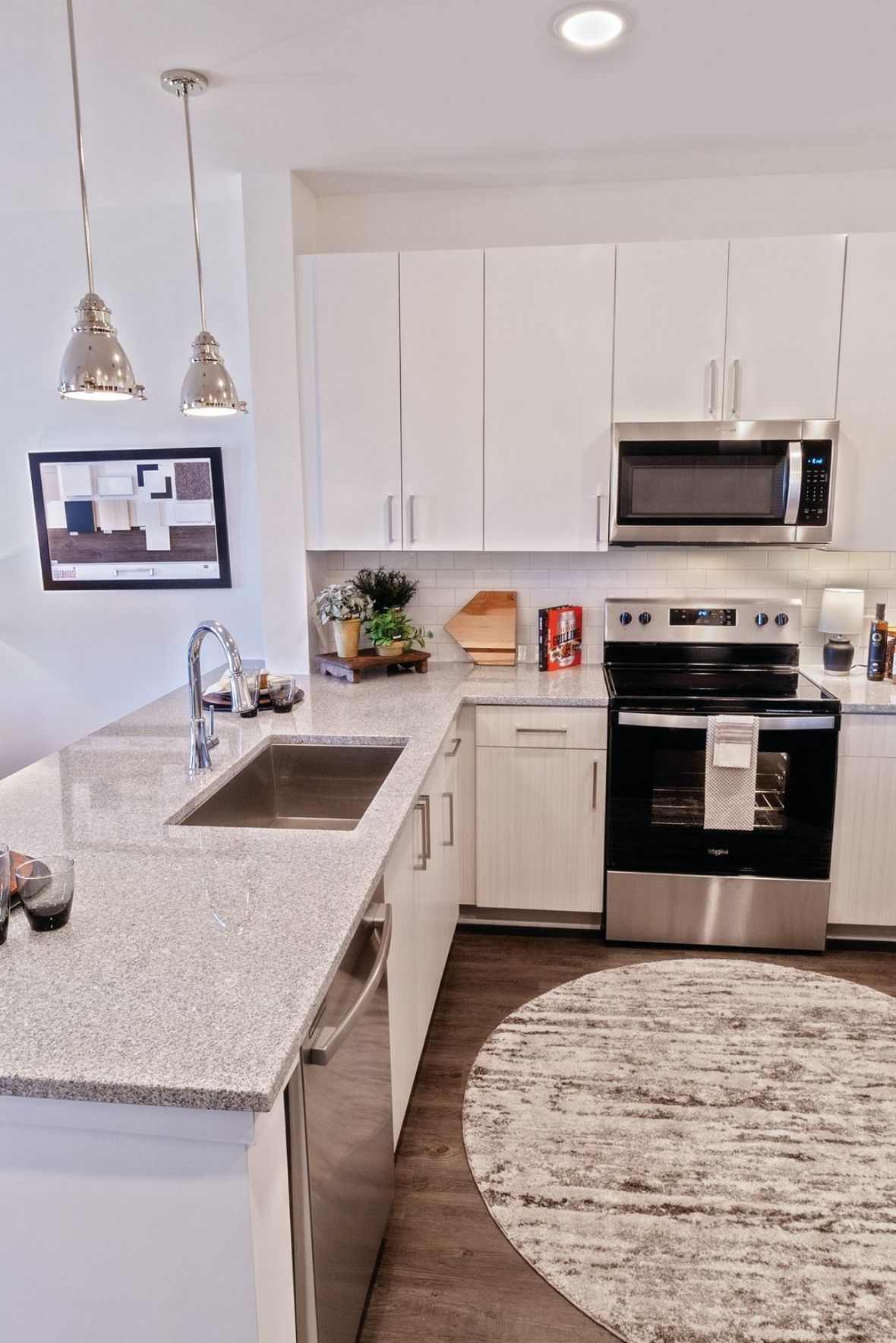 Modern kitchen with white cabinets, stainless steel appliances, and a round rug on a wood floor at The Fieldhouse Apartments.