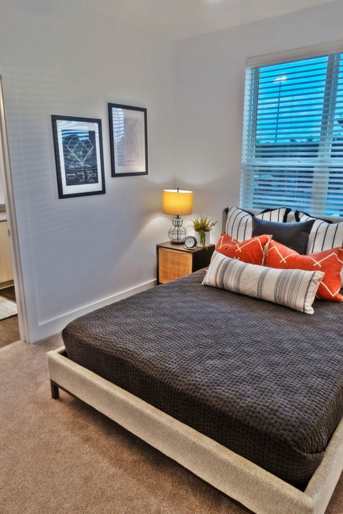 Modern bedroom with a double bed, orange pillows, two bedside tables, lamps, and an adjacent bathroom at The Fieldhouse Apartments.