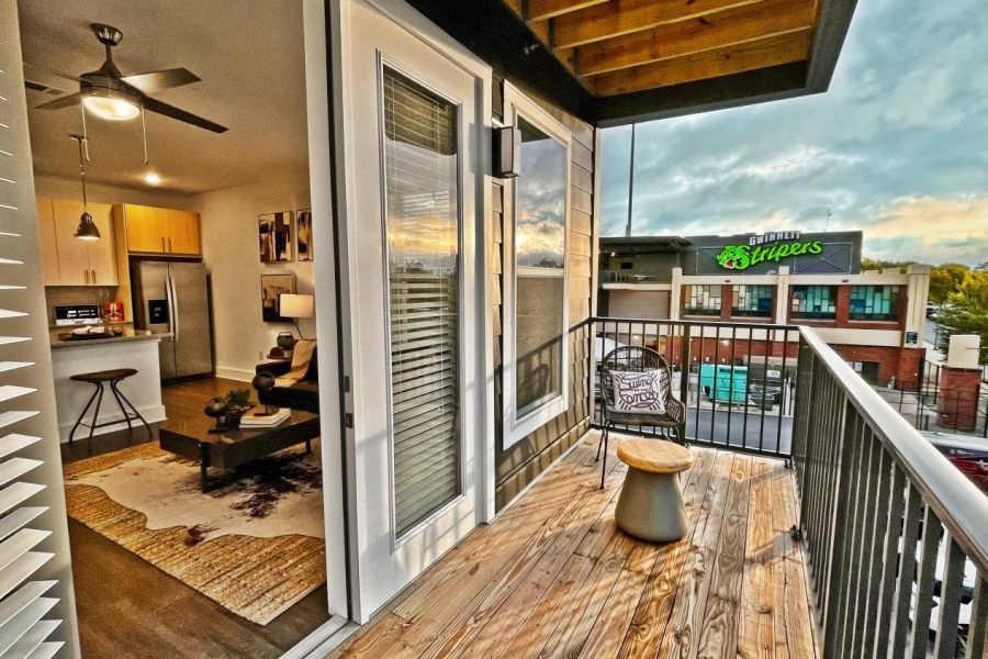 Modern apartment balcony with wooden floor, chair, and sunset view of a street and a grocery store  at The Fieldhouse Apartments.