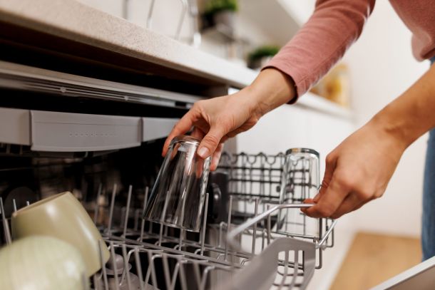Person loading clear glasses into a dishwasher in a modern kitchen.