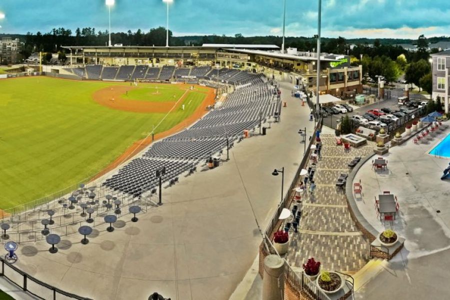 A panoramic view of a baseball stadium beside a large outdoor pool and apartment buildings at dusk.