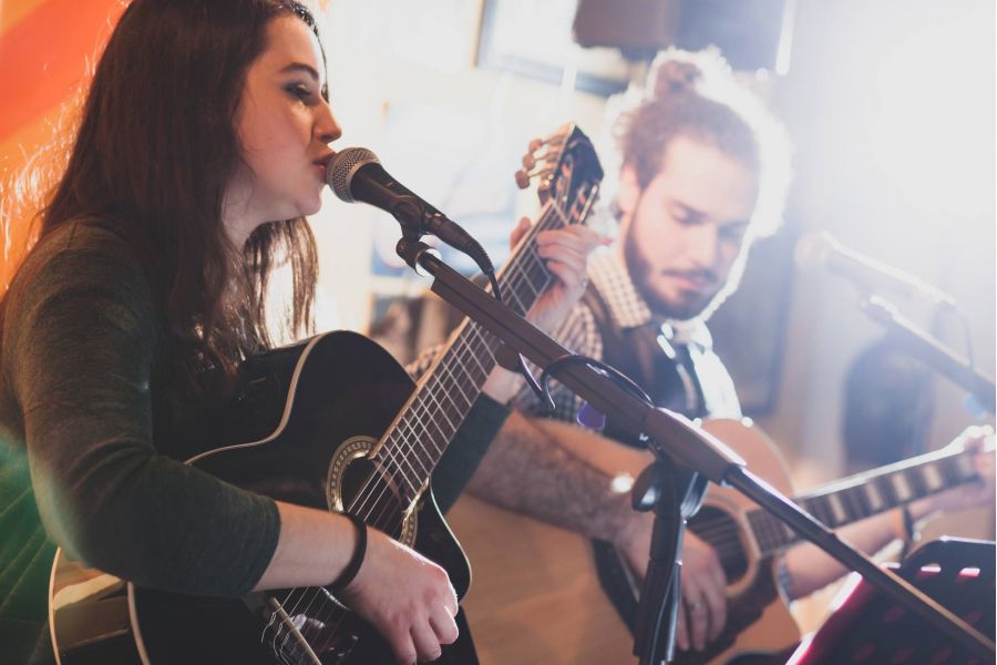 Woman singing and playing guitar with a man also playing guitar beside her during a live performance.
