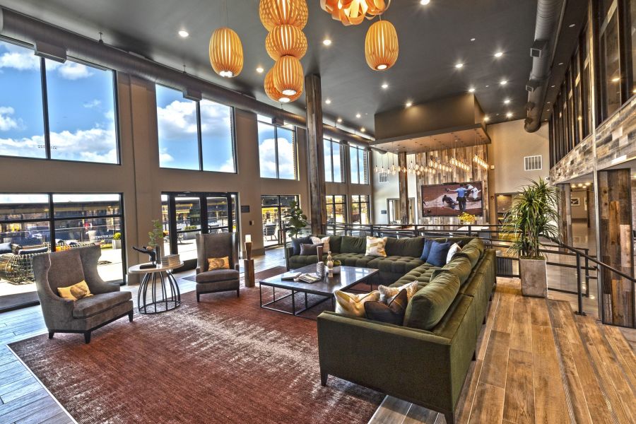 Spacious modern lounge with large windows, green sofa, armchairs, and hanging pendant lights at The Fieldhouse Apartments.