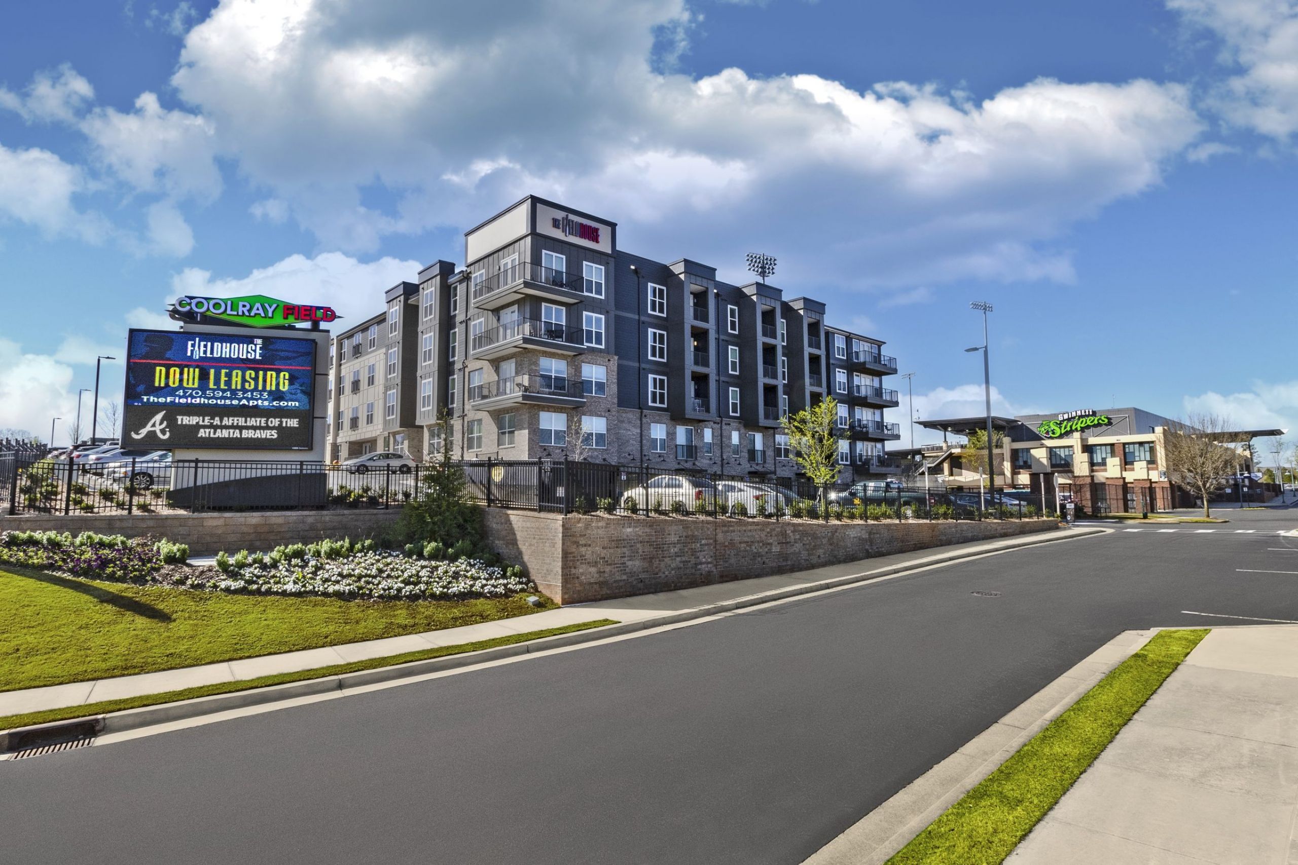 The Fieldhouse Apartments building and stadium with a digital sign showing leasing information, under a blue sky with clouds.