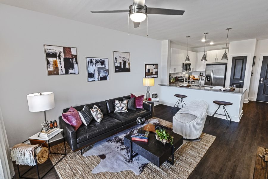 Modern living room with black sofa, armchair, coffee table, and open kitchen with bar stools in the background  at The Fieldhouse Apartments.